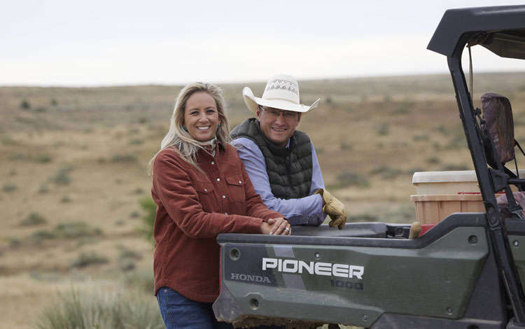 Shali & her husband posing for the camera leaning up against a pioneer four by four.